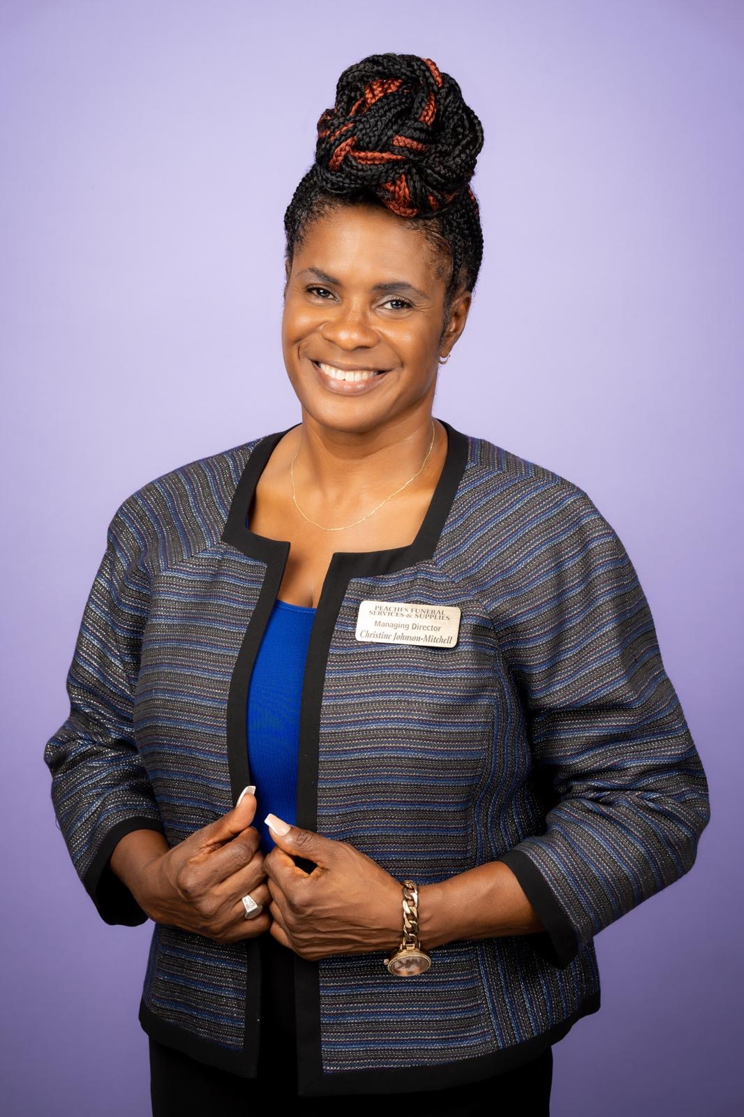 Christine L Johnson, Managing Director of Peaches Funeral Services & Supplies, smiling in a striped jacket against a lavender background